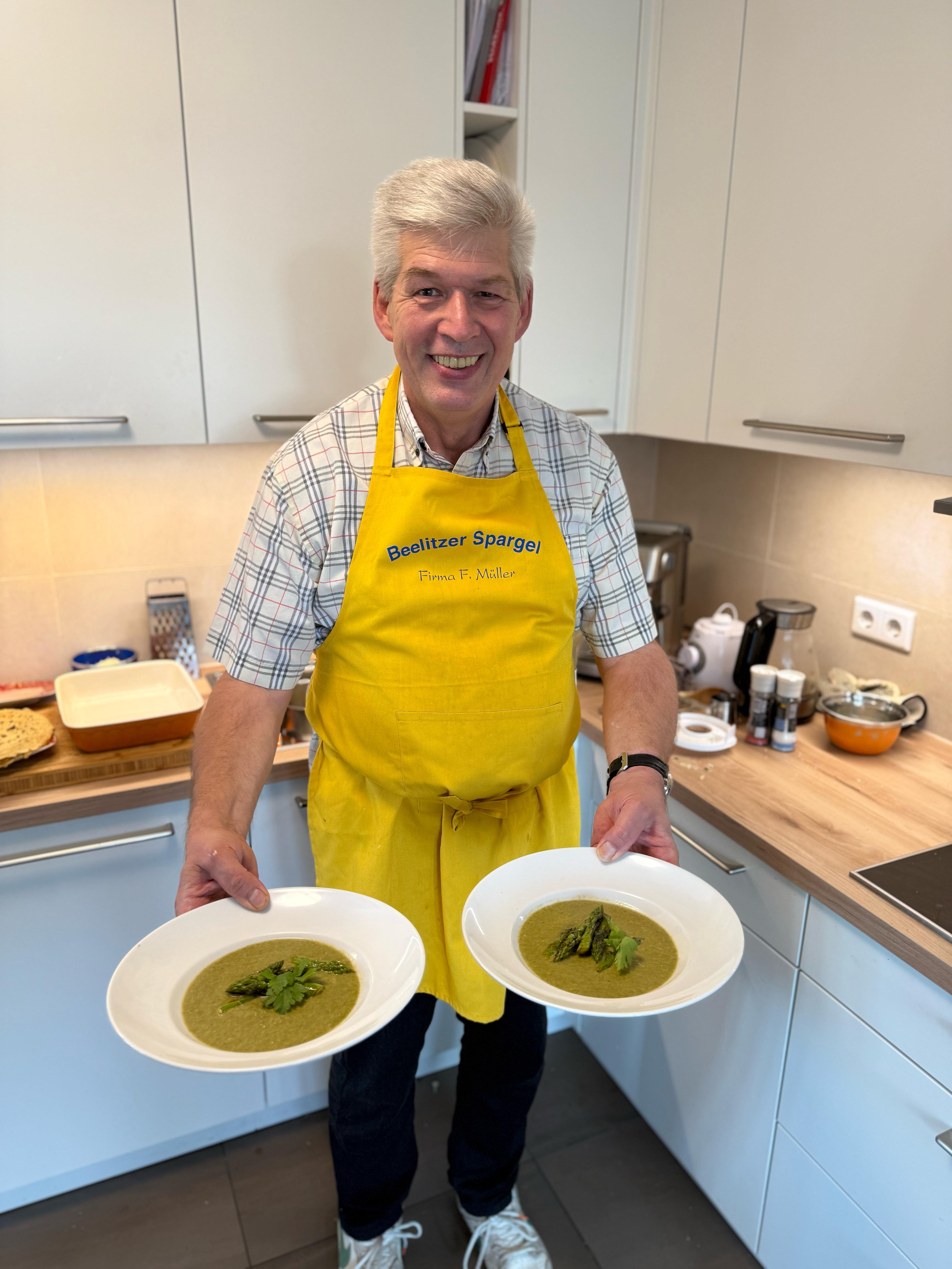 Eine Person in einer Küche hält grüne Spargelsuppe